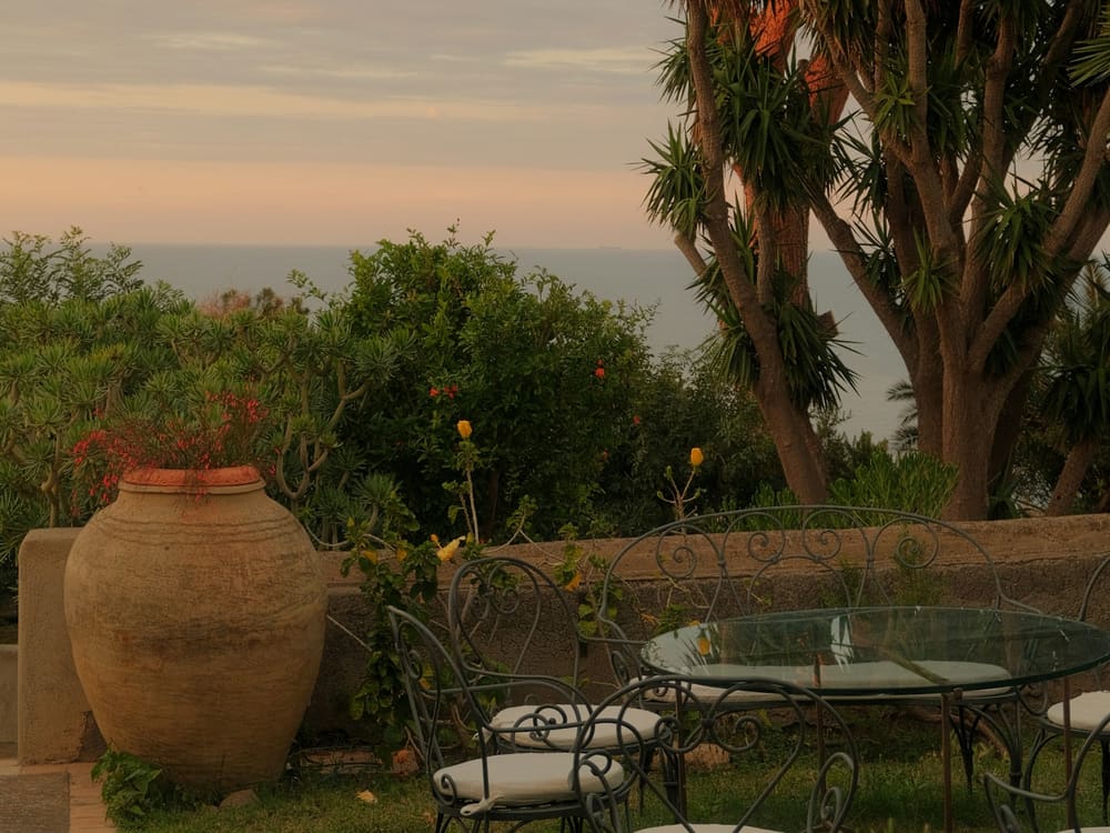 Jardin face à la mer au crépuscule, avec jarre en terre cuite et salon en fer forgé